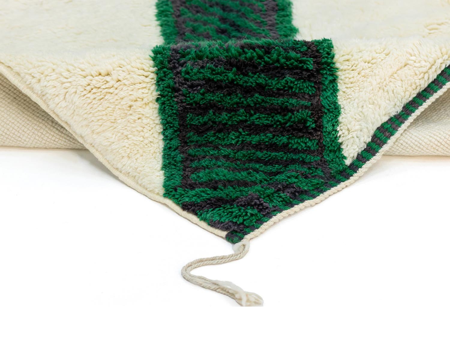 A corner of the cream and green textured Moroccan rug is folded over, revealing a tassel.