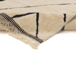 Close-up of a rug with black geometric lines and fringe on the edge, partially folded over at the corner. The intricate design adds a touch of elegance to any room.