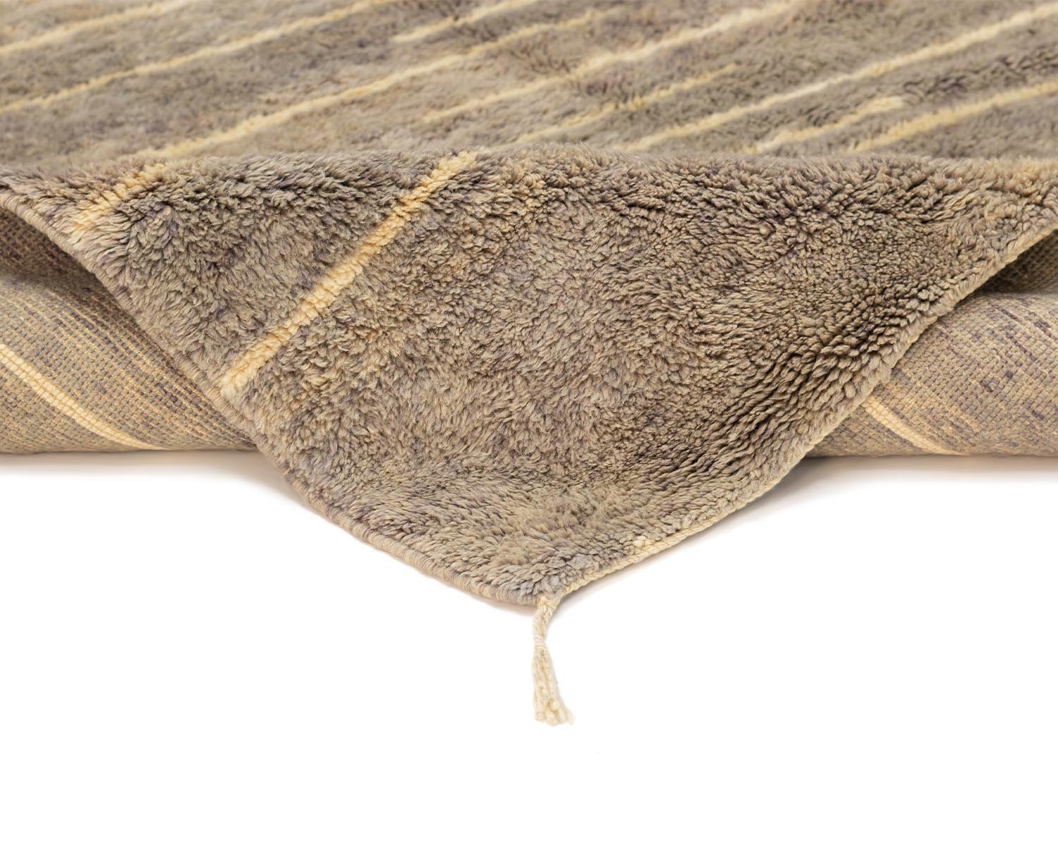 A close-up of a folded fuzzy brown and beige striped rug with its corner turned over reveals the intricately woven underside.