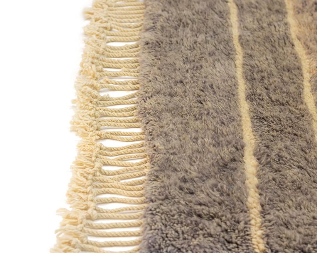 This close-up captures the textured allure of a gray shaggy rug, accentuated by beige fringes edging its perimeter. Its intricate fibers weave together for a captivating design.