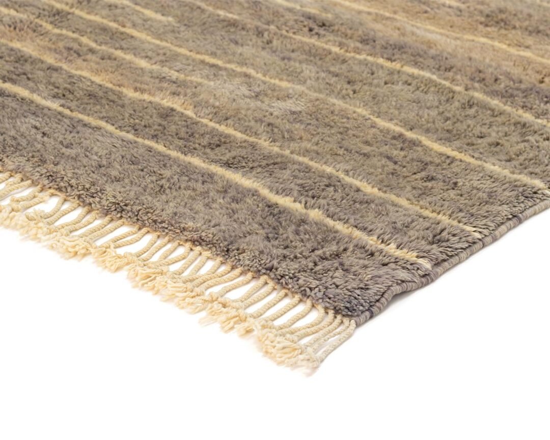 A close-up of a beige and brown striped rug with fringe on one side is displayed against a pristine white background, showcasing its intricate texture.