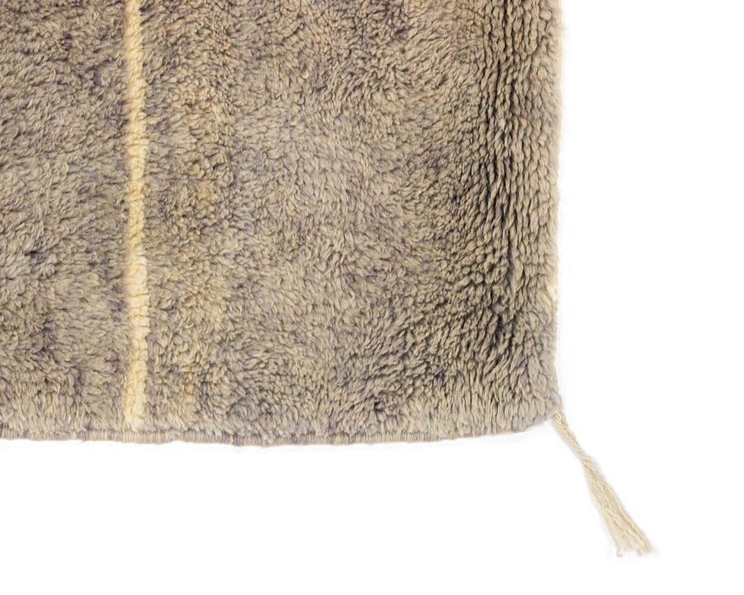 A cozy close-up of a beige and gray shaggy rug with a visible fringe in the bottom right corner, featuring a subtle vertical line that adds to its textured allure.