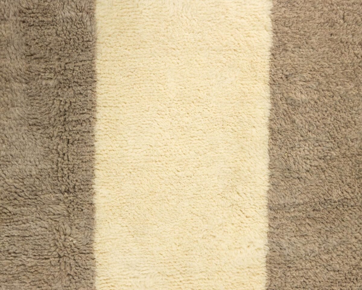 A close-up of a textured rug features three striking vertical stripes: two in rich brown bracketing a cream stripe in the center.