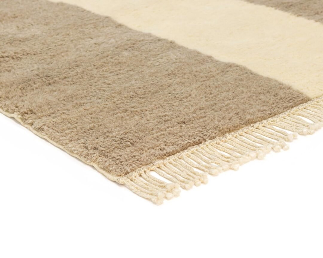 A close-up of a cozy, beige and brown striped rug showcases its fringed edges on one side.