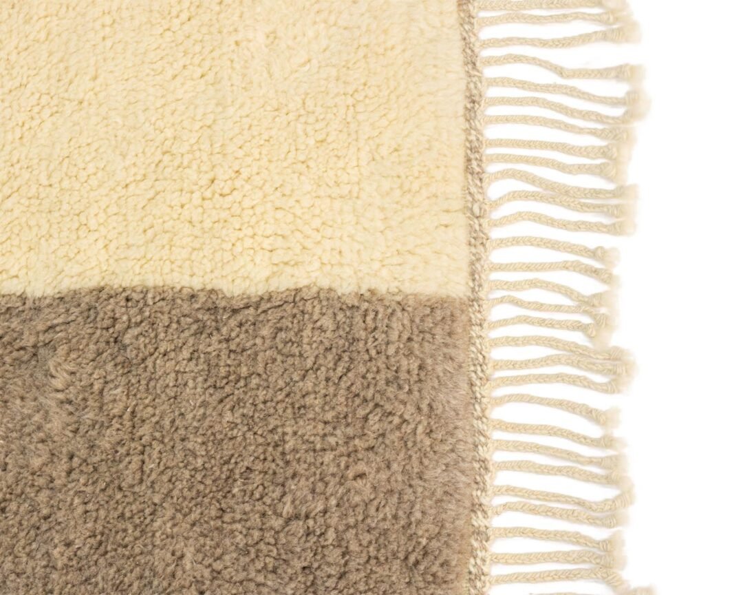 This close-up showcases a textured rug with fringe, featuring a beige and brown color block design. The intricate patterns and warm tones add an inviting touch to any space, blending rustic charm with elegance.