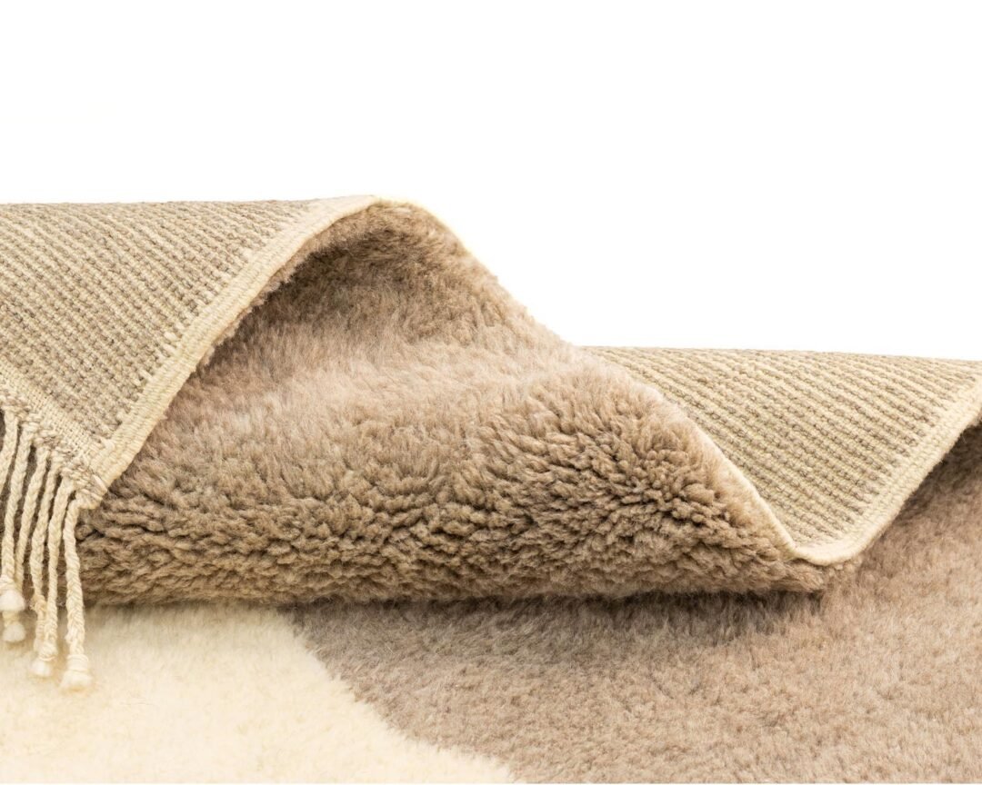 Close-up of a folded beige area rug highlighting its woven and fluffy textures, accented by fringes on one edge.