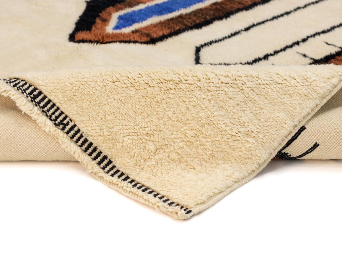 The corner of a beige rug is folded over, revealing a striped edging. A hint of geometric design in blue and brown adorns the surface, adding a touch of sophistication to any room.