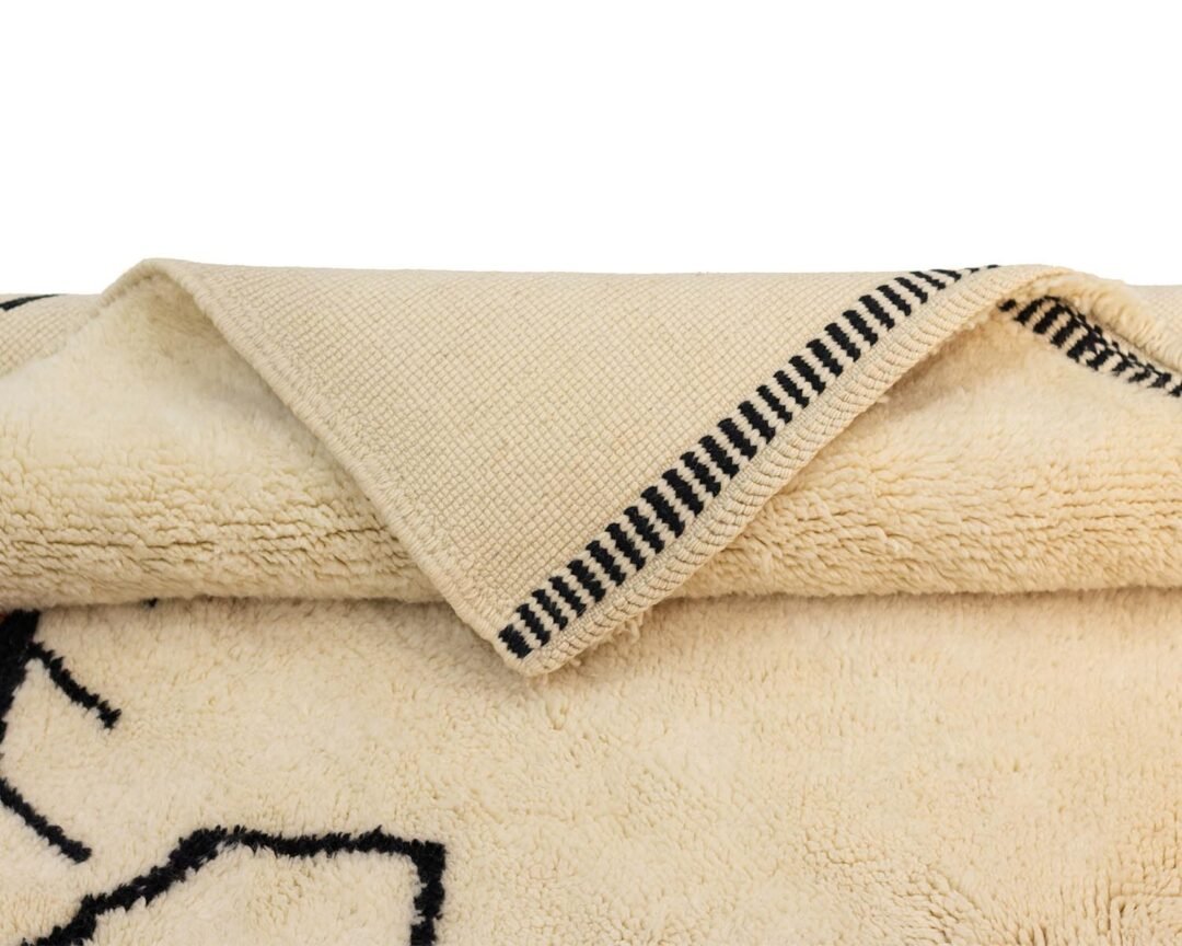 A folded beige fleece with black geometric patterns along the edge and a striped border offers warmth and style, blending seamlessly into any cozy space.