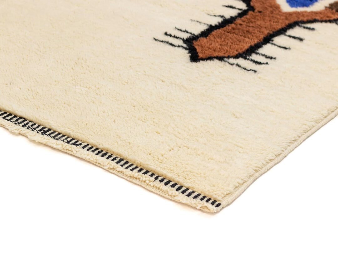 Close-up of a beige rug corner showcasing a brown and blue geometric pattern, beautifully accentuated by a striped black and white border.