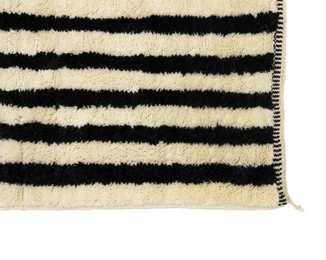 A beige rug with black horizontal stripes and a stitched border is showcased.