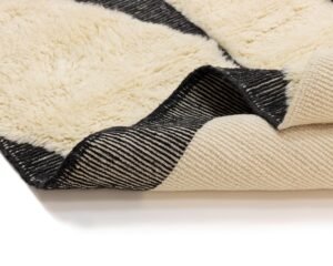Close-up of a folded black and beige striped rug with intricate stitching.