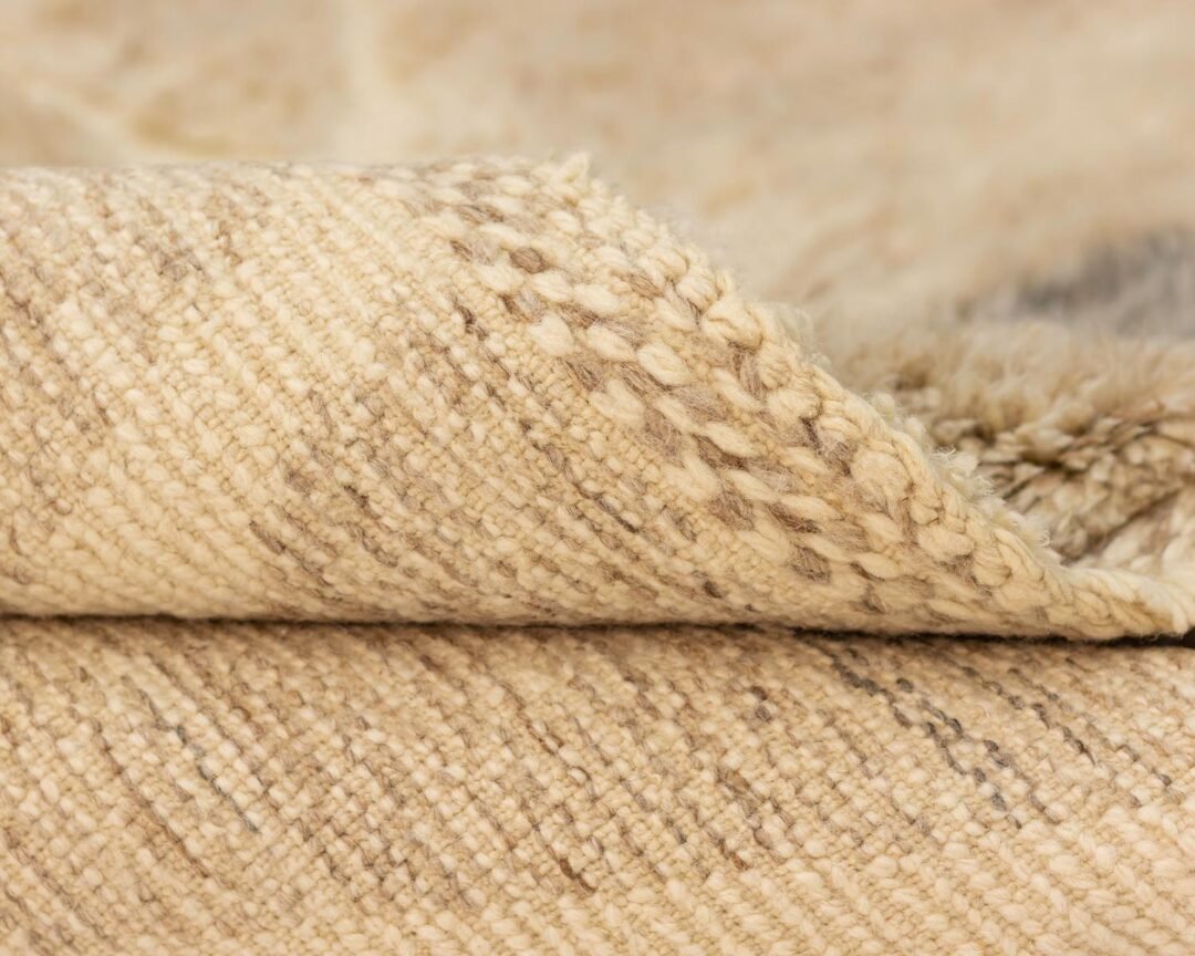 Close-up of a folded beige woven fabric with a textured surface and subtle, light brown designs. This intricately crafted material showcases elegance and sophistication, making it perfect for various creative projects or home decor applications.