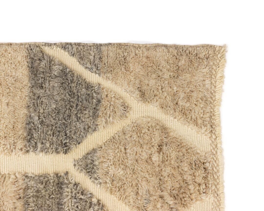 A close-up showcases the intricate beige and gray geometric pattern of the shag rug, highlighting its textured, fluffy surface and edge detail for a cozy addition to any room.