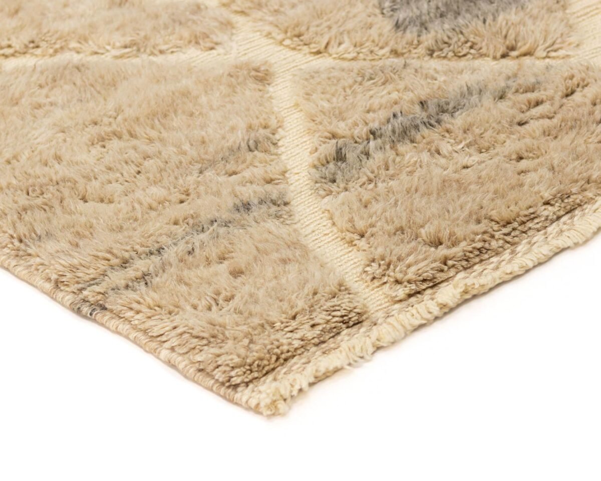 A close-up reveals the intricate corner of a beige shaggy rug adorned with a subtle diamond pattern and delicate light grey streaks, creating an elegant texture.