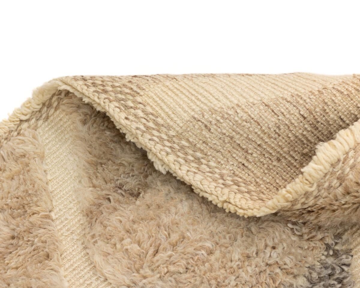 A textured rug showcases its beige and brown woolly surface in a close-up view, partially folded to reveal a woven underside.