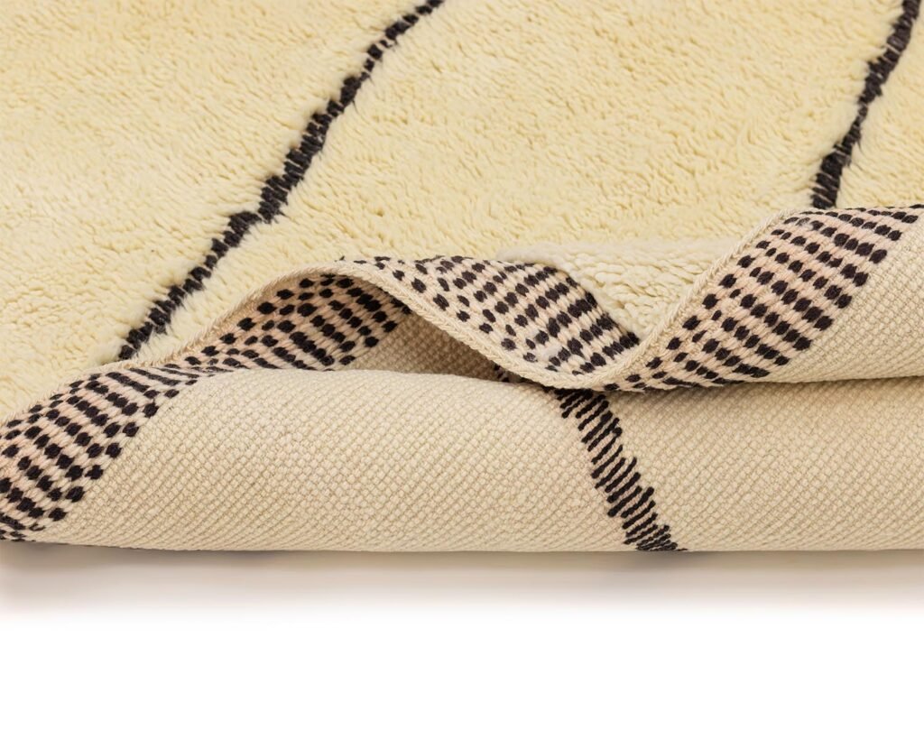 A close-up of an area rug showcases its beige base with striking black lines, and a folded corner reveals a fascinating dotted pattern on the underside, offering a modern touch to any space.