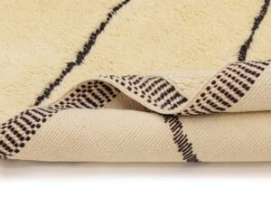A close-up of an area rug showcases its beige base with striking black lines, and a folded corner reveals a fascinating dotted pattern on the underside, offering a modern touch to any space.