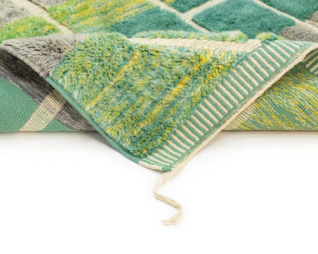 This green and yellow textured Moroccan rug is partially folded, showcasing its striped underside. A loose string graces the edge, adding to its charm.