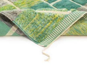 This green and yellow textured Moroccan rug is partially folded, showcasing its striped underside. A loose string graces the edge, adding to its charm.