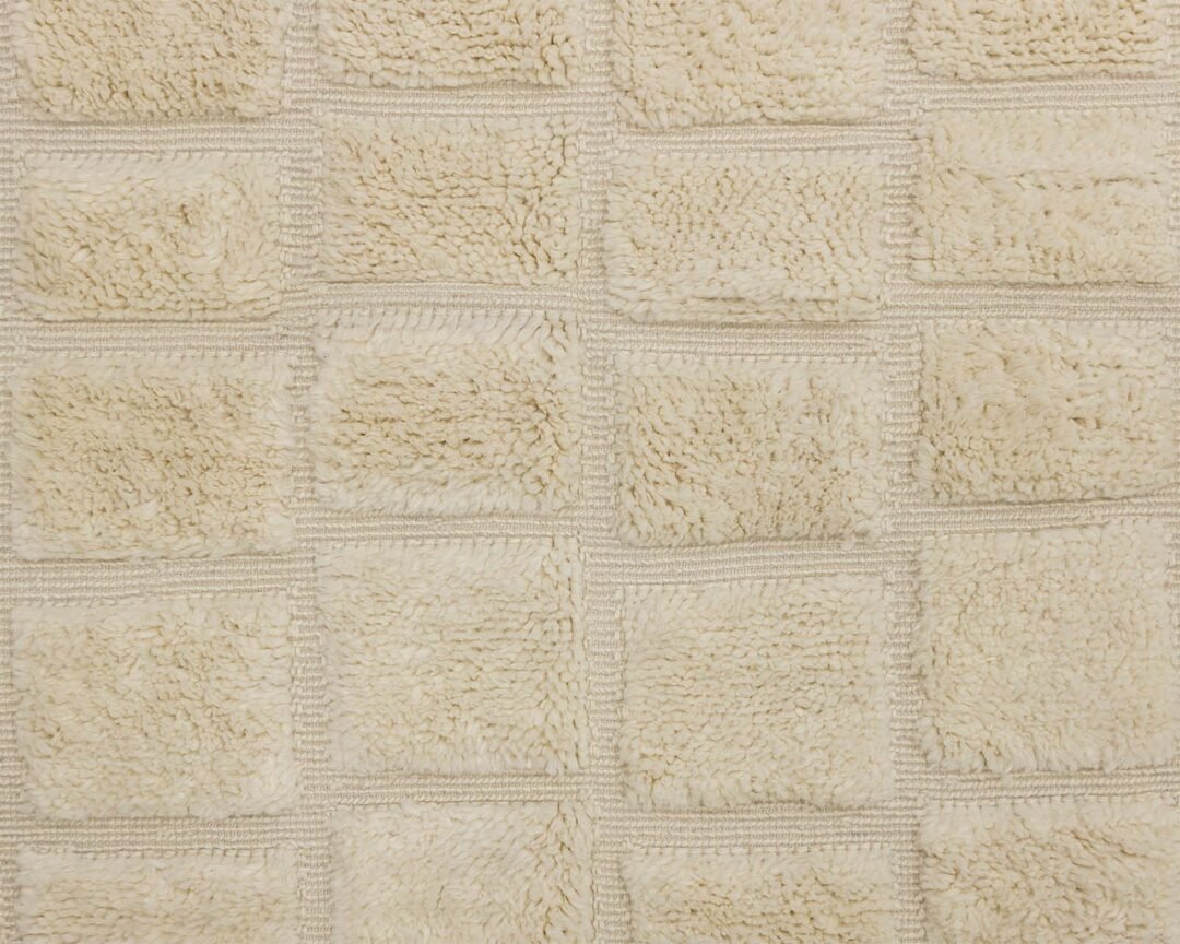 Close-up of a textured beige fabric, reminiscent of a hand-knotted Moroccan rug, with a grid pattern of raised square sections.