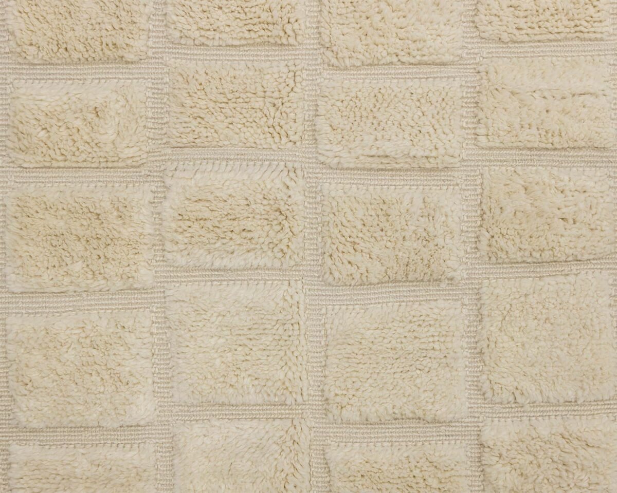 Close-up of a textured beige fabric, reminiscent of a hand-knotted Moroccan rug, with a grid pattern of raised square sections.