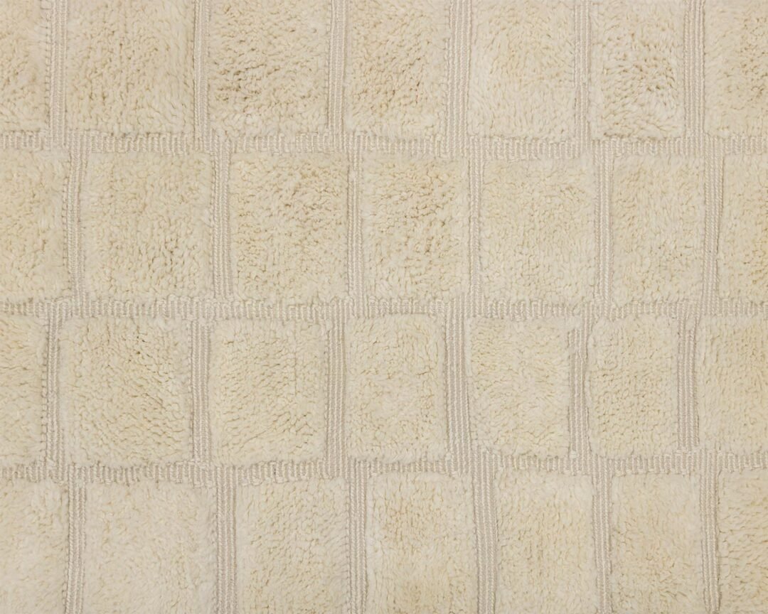 Close-up of a beige textured fabric resembling a Moroccan rug, with a checkered pattern consisting of rectangular patches.