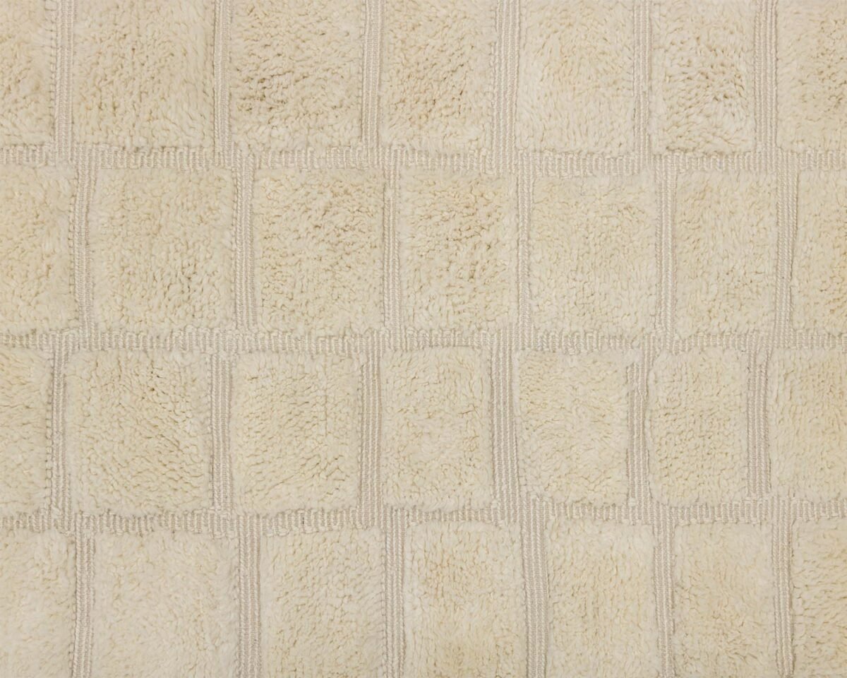 Close-up of a beige textured fabric resembling a Moroccan rug, with a checkered pattern consisting of rectangular patches.