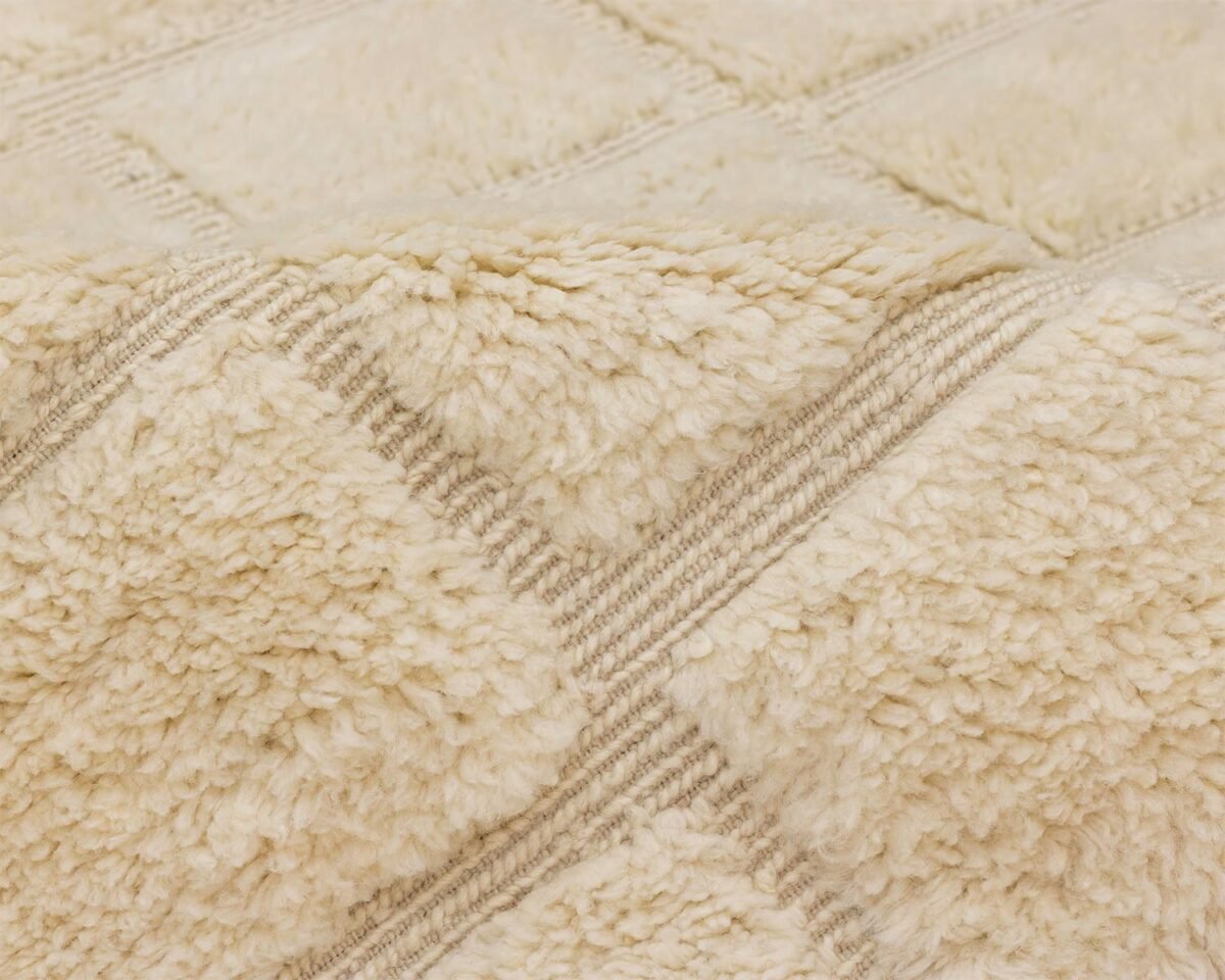 Close-up of a textured beige fabric resembling a luxury rug with a plush, fluffy surface and patterned stitching.