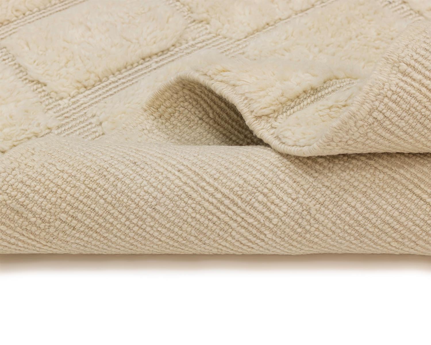 Close-up of a folded beige textured bath mat, showcasing its soft, quilted surface and ribbed underside reminiscent of a luxury rug.