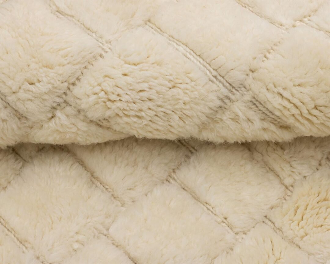 A close-up of a beige fleece fabric showcases a quilted diamond pattern, reminiscent of an artisanal rug. The soft and fluffy texture invites warmth and comfort.