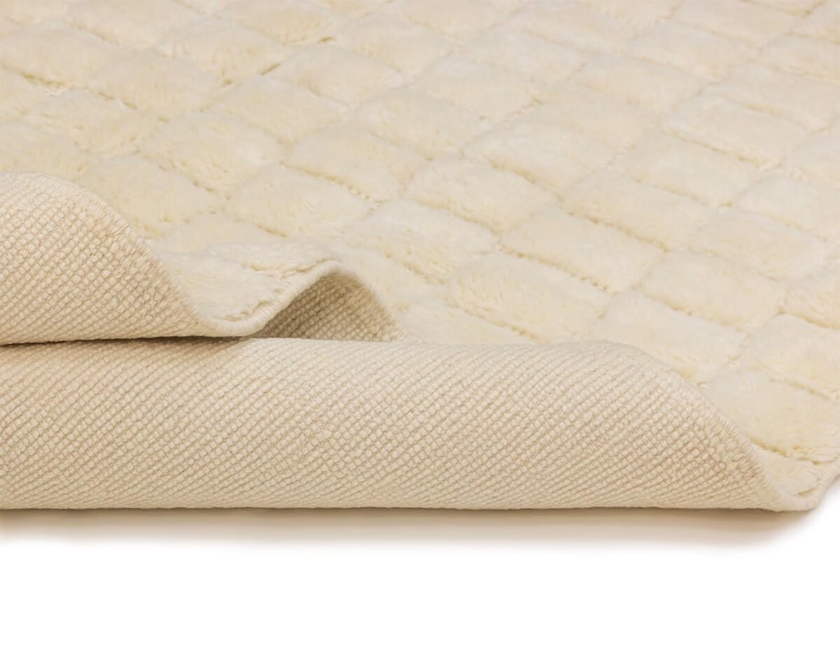 Close-up of an artisanal beige area rug with a folded corner, showcasing its soft pile surface and woven underside.