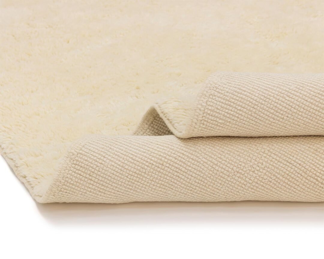 A folded beige rug lies on a plain background, with its soft, fluffy side invitingly on display while a textured underside peeks out.