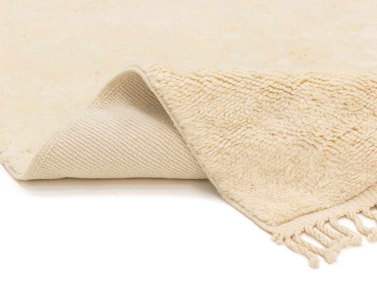 Close-up of a beige rug with fringe, partially folded to reveal its woven underside, adding a subtle touch of elegance.