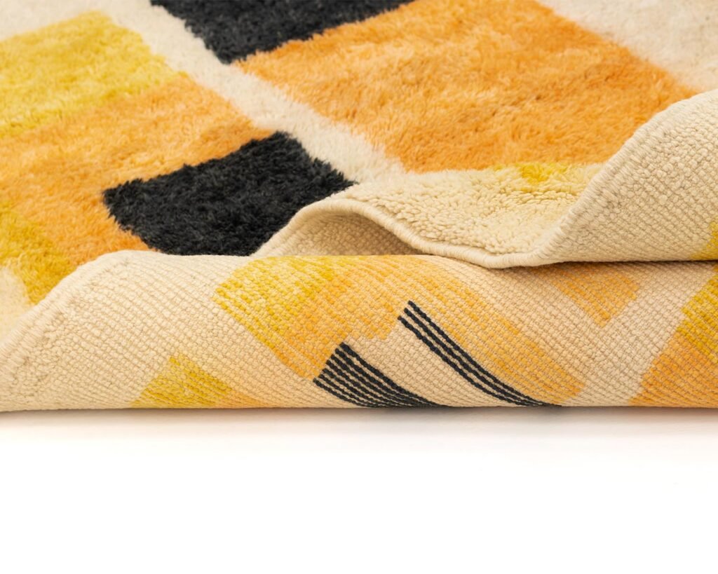 Close-up of a luxury, hand-knotted rug featuring a geometric pattern with yellow, orange, and black rectangles on a beige background.