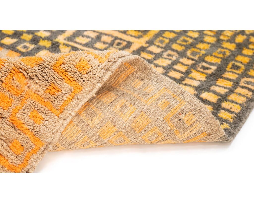 Close-up of a folded corner of a patterned rug, showcasing geometric designs in vibrant orange and grey tones.