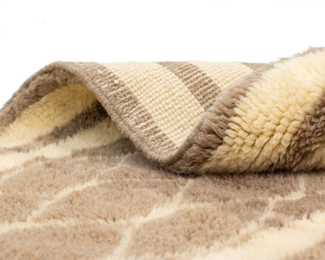 A close-up of a beige and brown patterned luxury rug folded over, revealing both the woven and fleecy sides reminiscent of a cozy Moroccan design.