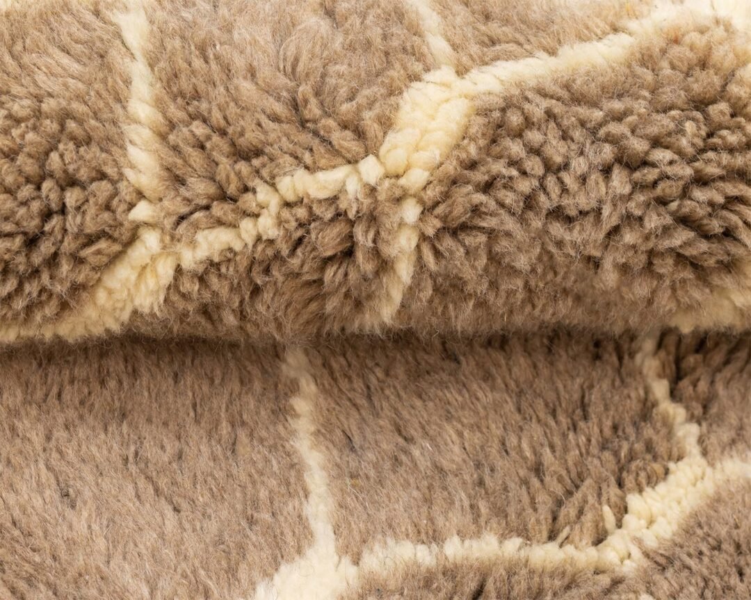 This close-up showcases a folded piece of brown and cream woolen fabric with a geometric pattern, reminiscent of the intricate designs found in a luxury Moroccan rug.