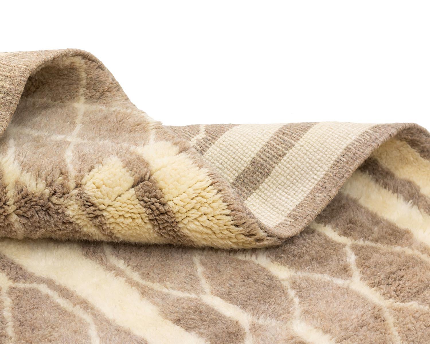 A close-up of a beige and brown patterned Moroccan rug with a fluffy texture, displaying its folded corner to reveal the underside.