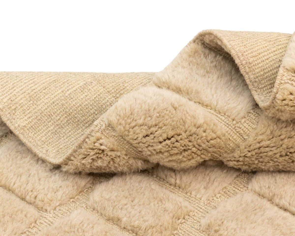 Close-up of a beige, textured fabric with a quilted pattern and soft, fuzzy surface, reminiscent of cozy interiors.