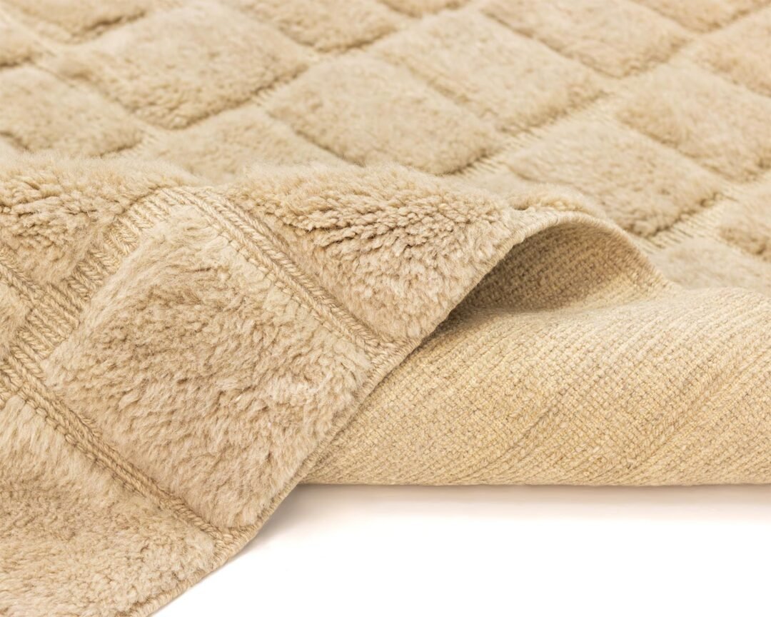 Get a closer look at this beige, textured bath mat, featuring a soft, plush side and a smooth, woven underside designed for comfort and style in any bathroom setting.