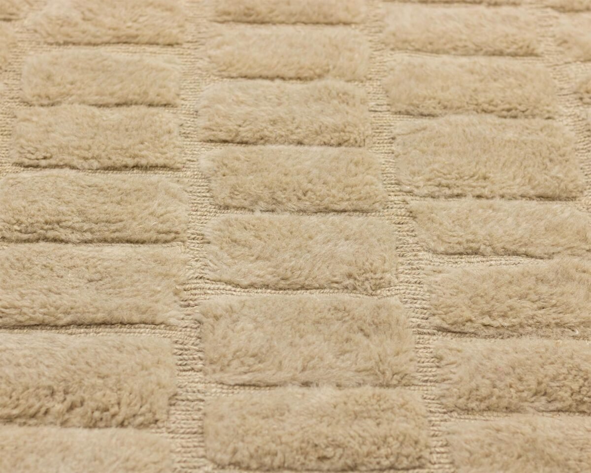 Close-up view of a beige textured fabric featuring a rectangular, raised, tufted pattern that adds depth and elegance.