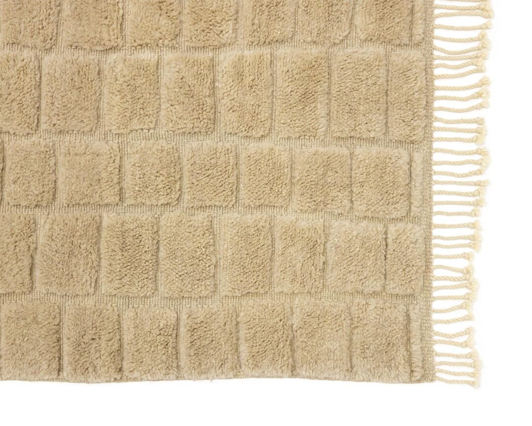 A beige textured rug features a grid pattern and fringes elegantly adorning the right side, adding a touch of sophistication to any room.