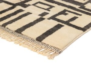 A beige and black geometric patterned rug with fringed edges rests against a white backdrop, adding an artistic flair to your space.