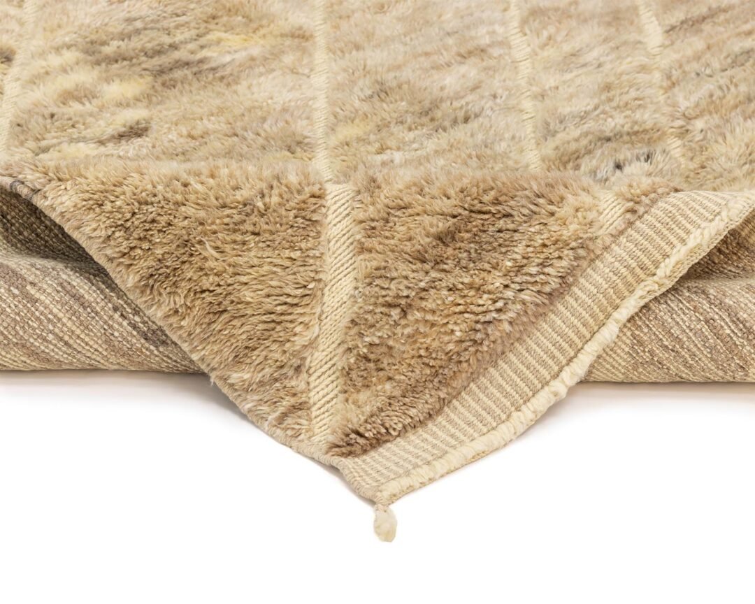 A close-up of a folded, beige, textured carpet showcases its fluffy surface and woven underside.