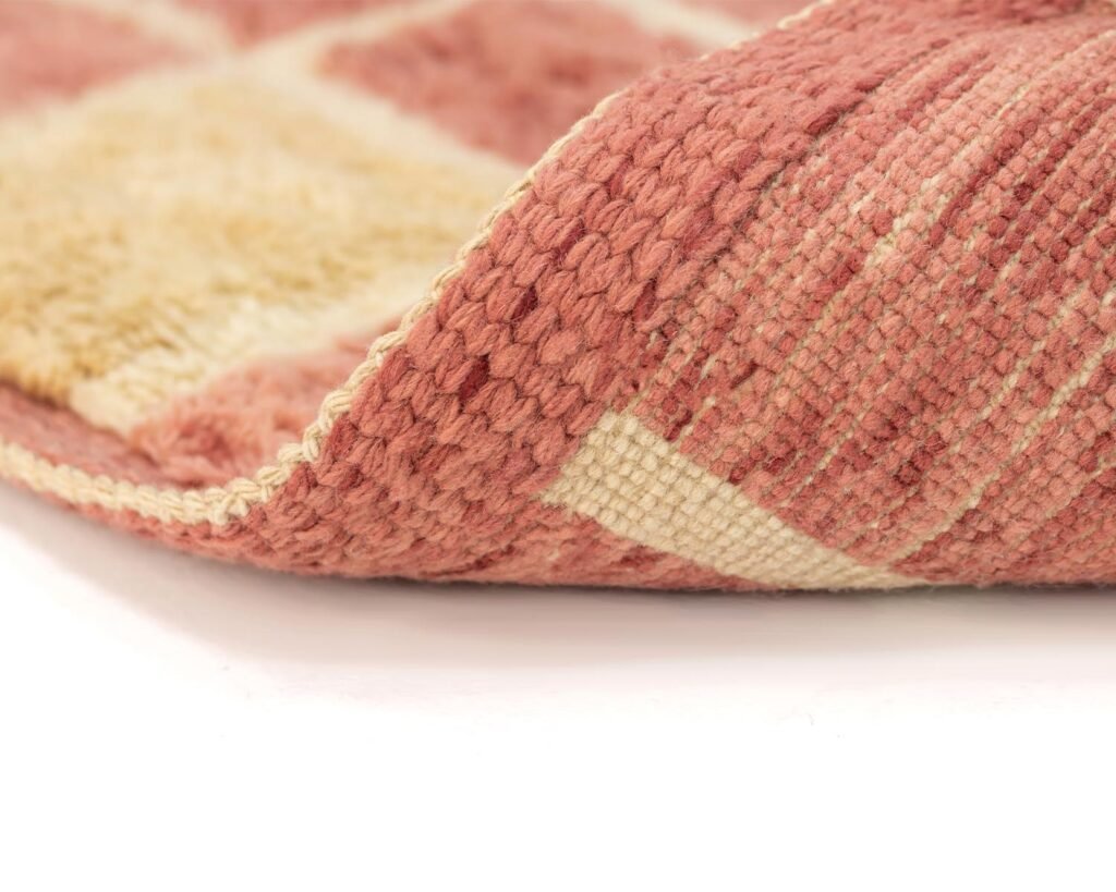 Close-up of a folded pink and beige woven rug showing its texture and pattern detail.