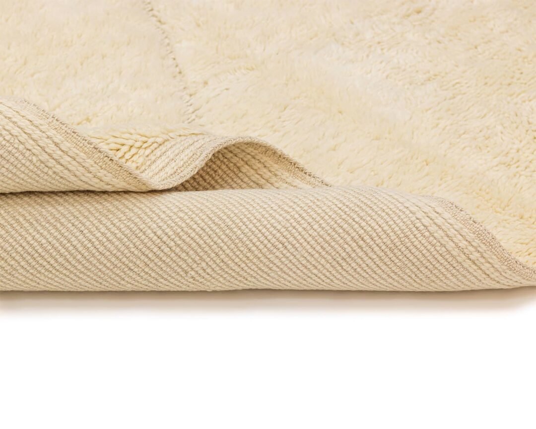 Close-up of a beige, luxury rug corner folded over, revealing the intricate woven underside and soft, fluffy surface.