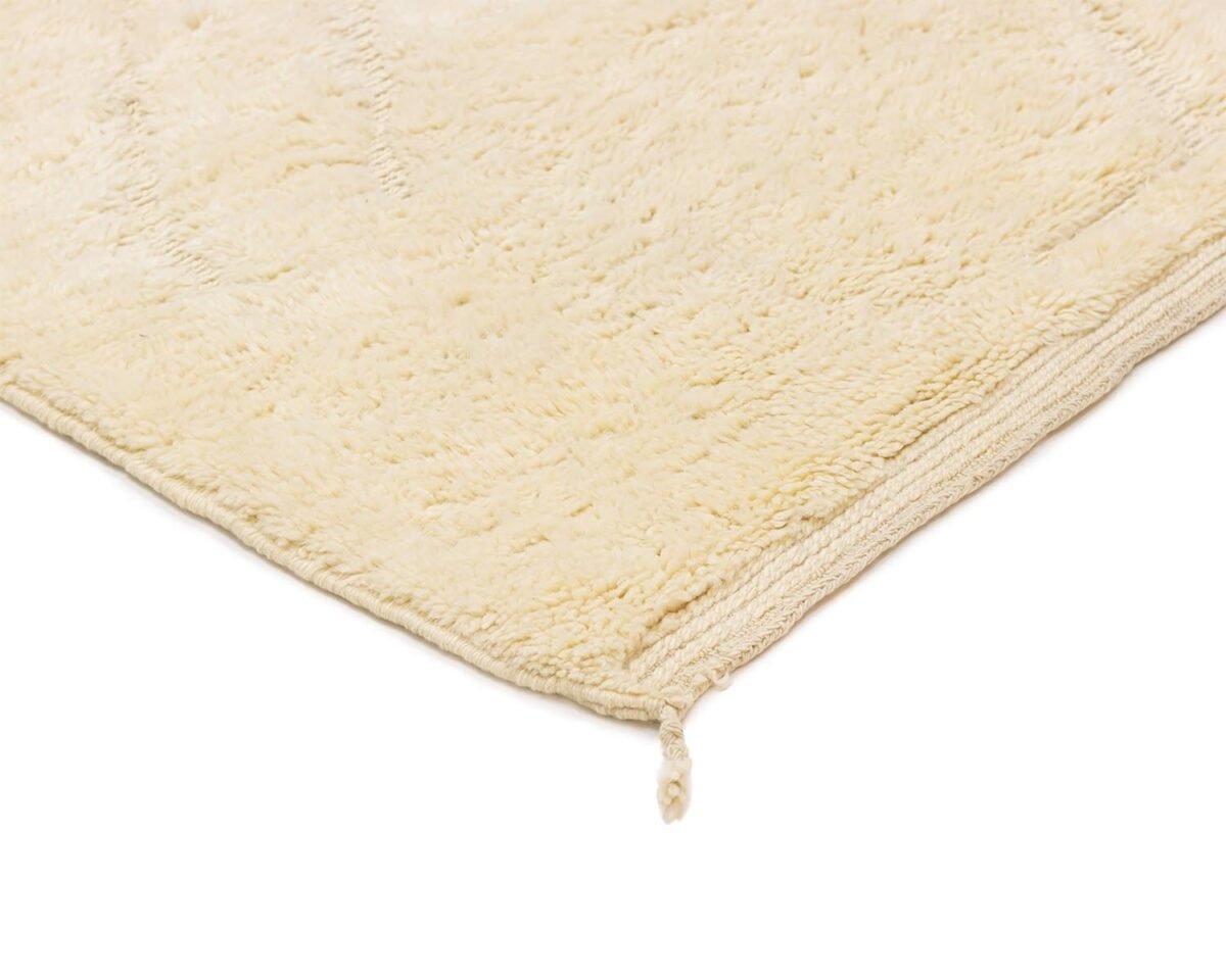 Close-up of the corner of a beige hand-knotted rug with a knotted tassel, elegantly displayed on a white background.