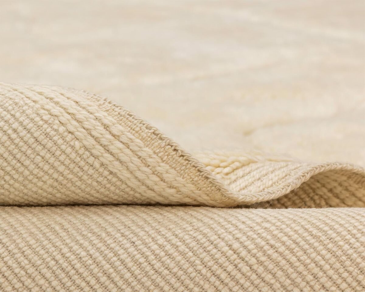 Close-up of a folded luxury rug, showcasing its textured surface and layered edge under soft lighting.