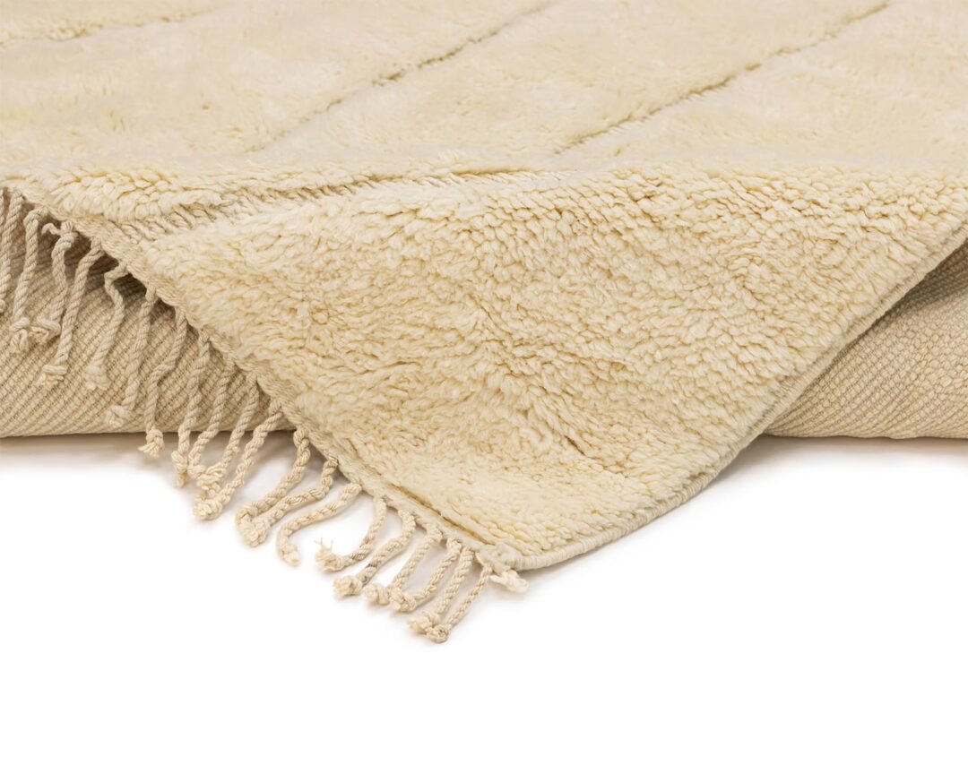 Close-up of a beige, fringed, textured Moroccan rug on a white background, showcasing its intricate design.