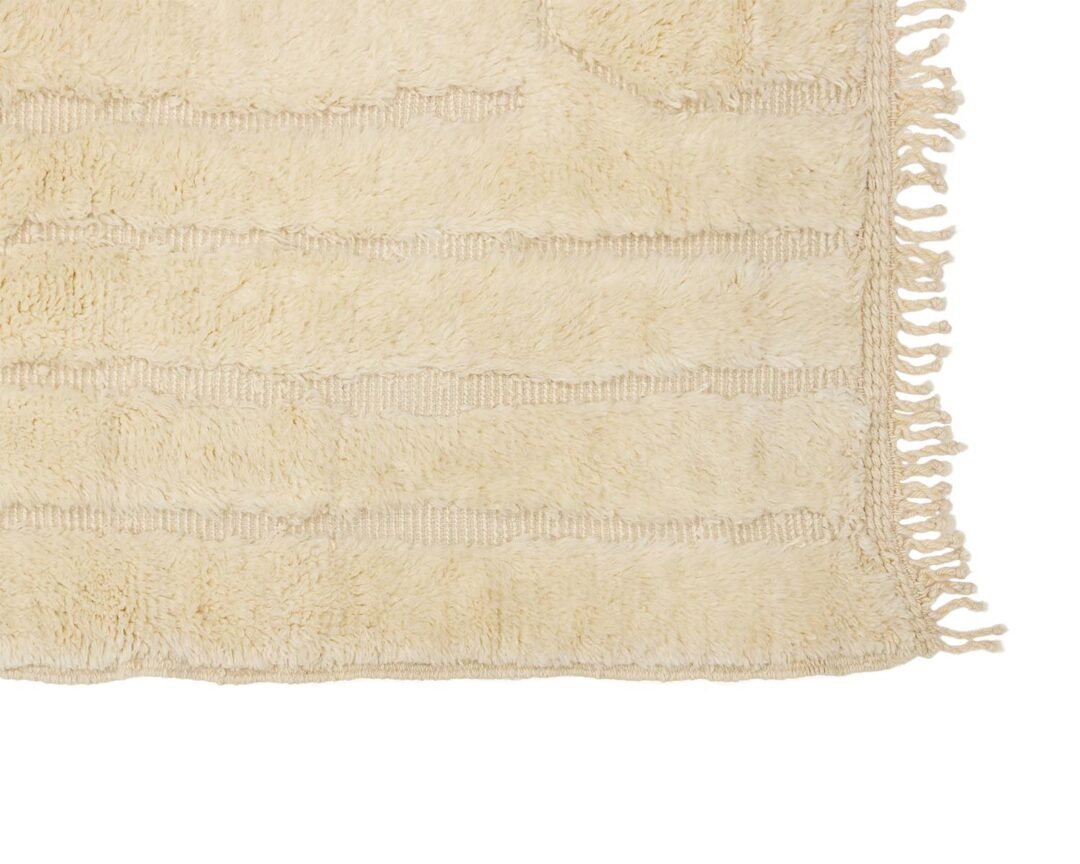 A close-up showcases a beige textured rug, intricately designed and featuring charming fringed edges on the right side.